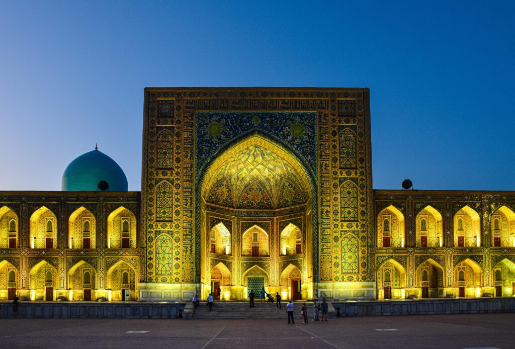 A stunning view of the Tilya-Kori Madrasah in Uzbekistan illuminated against a twilight sky, showcasing intricate architecture.